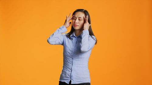 Portrait of young woman standing against yellow background