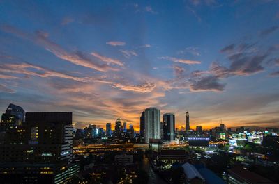 Illuminated buildings in city against sky during sunset