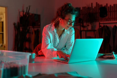 Young entrepreneur girl self-employed dressmaker and studio owner work on laptop in workshop atelier
