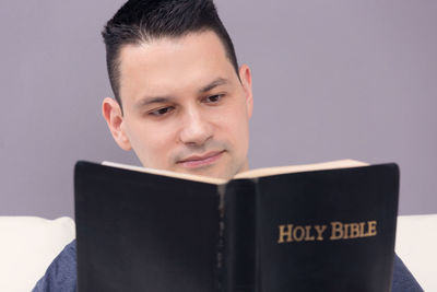 Portrait of man holding book against gray background