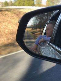 Reflection of boy in side-view mirror of car