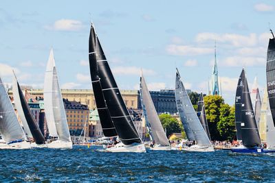 Sailboats in river by buildings against sky