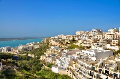 High angle view of townscape by sea against clear blue sky