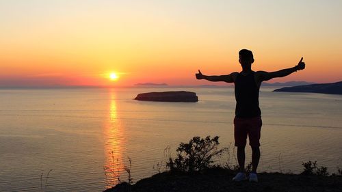 Silhouette man standing on rock by sea against sky during sunset