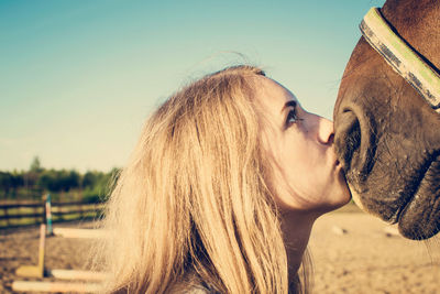 Close-up of young woman kissing horse against clear sky