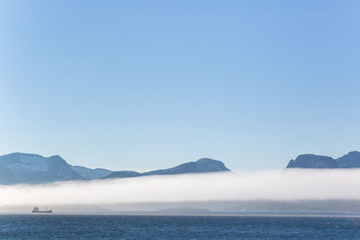 Scenic view of sea and mountains against clear sky during foggy weather