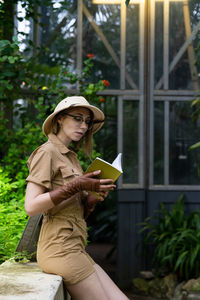 Side view of woman reading book in greenhouse