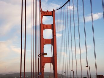 Low angle view of suspension bridge against cloudy sky