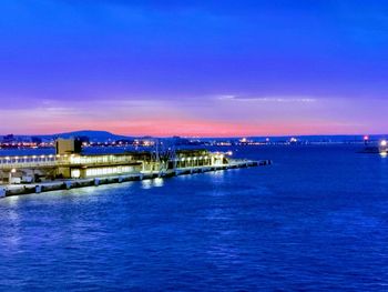 Illuminated bridge over sea against sky at sunset