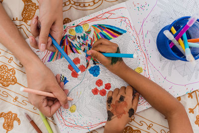 Close-up of the hands of a caucasian mom and hispanic daughter. they are painting while they are lying in the bed.