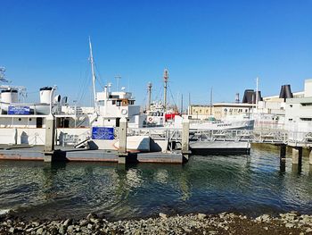 Boats in harbor against clear blue sky