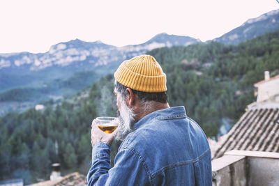 Side view of a happy man contemplating the views with a cup of tea on a mountain balcony