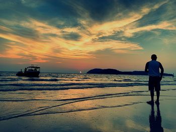 Rear view of man standing on beach against sky during sunset