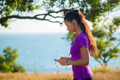 Young woman using mobile phone while listening music by sea