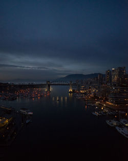 Illuminated city by sea against sky at dusk