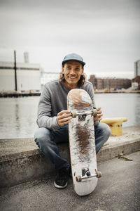 Portrait of smiling man with skateboard against canal