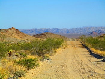 Dirt road leading towards mountains against clear blue sky