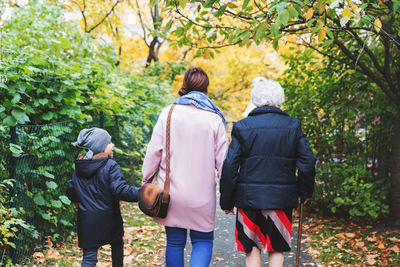 Rear view of senior woman walking with daughter and great grandson in park during autumn