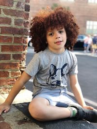 Portrait of a smiling girl sitting against brick wall