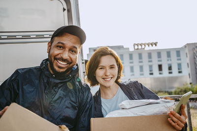 Portrait of smiling male and female delivery coworkers carrying cardboard boxes