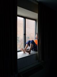 Full length of boy sitting by window at home