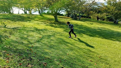 Boy running on field against trees