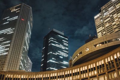 Low angle view of illuminated modern buildings against cloudy sky at night