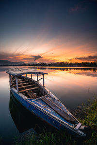 Boat moored in lake against sky during sunset