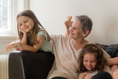 Smiling grandmother with granddaughters on sofa at home