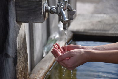 Cropped hands of woman holding falling water from faucet outdoors