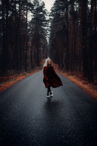 Woman walking on road amidst trees in forest