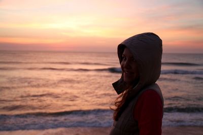 Young woman standing at beach against sky during sunset