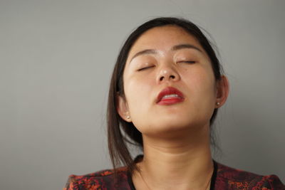 Young woman with eyes closed standing against white background