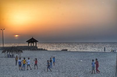 People on beach against sky during sunset