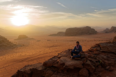 Woman sitting on rock at desert against sky