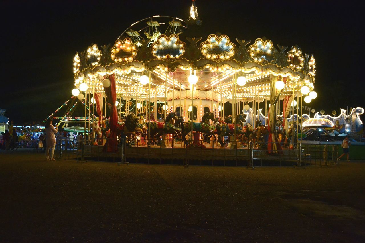 PEOPLE AT AMUSEMENT PARK RIDE AGAINST SKY AT NIGHT