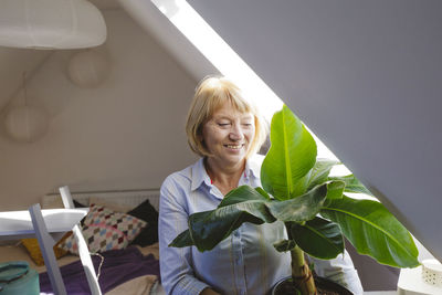 Happy senior woman with banana plant sitting in bedroom