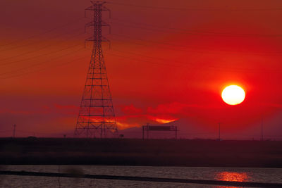 Silhouette electricity pylon against orange sky