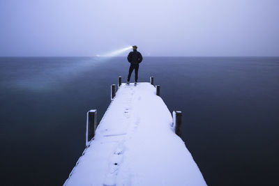 Tourist with headlamp admiring lake standing on jetty in winter, walchensee, bavaria, germany