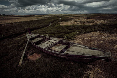 Abandoned boat moored on land against sky