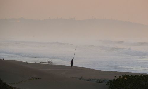 Man fishing in sea against sky