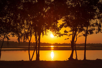 Silhouette trees by lake against sky during sunset