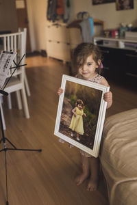 Young barefoot girl with wispy hair holding framed picture of herself