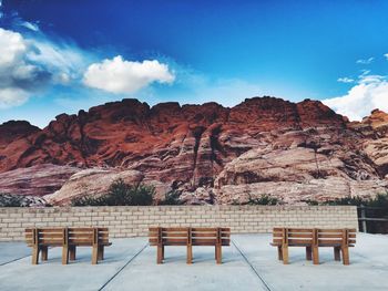 Empty benches in front of sandstone mountains against cloudy sky