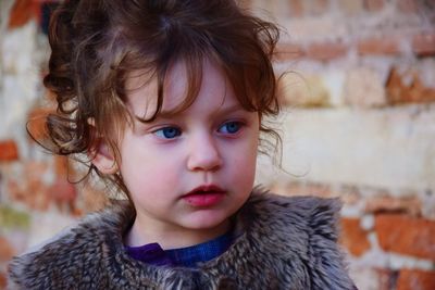 Cute girl looking away against brick wall