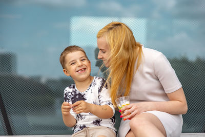 Happy blond woman and little boy sitting on terrace and eating sweets. mother and son 