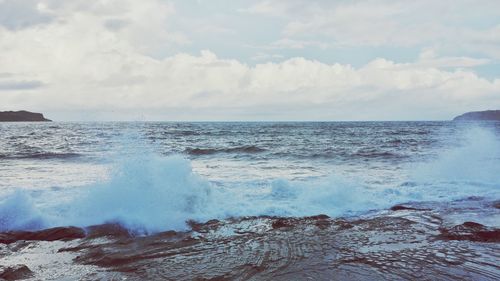 Waves splashing on rocky coastline against sky