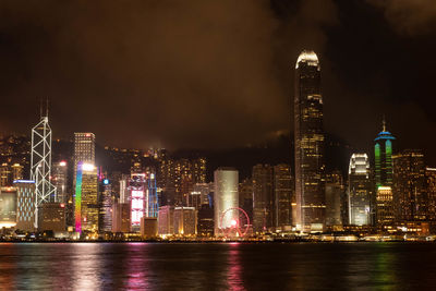 Illuminated buildings by river against sky at night