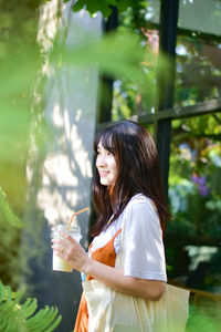 Side view of young woman standing against plants