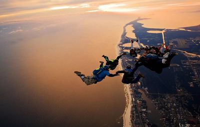 People skydiving over landscape during sunset